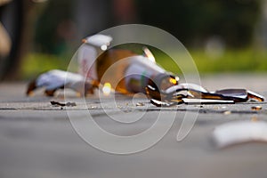 Bottle of beer, soda or drugs from dark glass is broken. Shattered beer bottle on ground in sunset light. Fragments of glass on