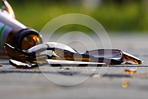 Bottle of beer, soda or drugs from dark glass is broken. Shattered beer bottle on ground in sunset light. Fragments of glass on