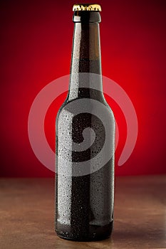 Bottle of beer with water drops on a stone table over red background