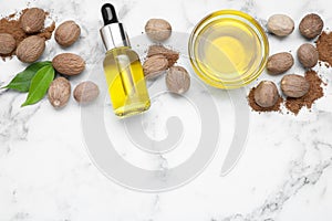 Bottle and bowl of nutmeg oil, nuts on white marble table, flat lay. Space for text