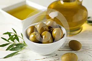 Bottle and bowl with olive oil, bowl with olives on wooden background