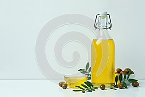 Bottle and bowl with olive oil, olives and twigs on white background