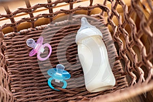 Bottle with breast milk and pacifiers for baby in straw basket.
