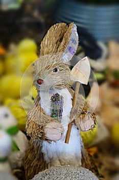 Bottle Brush toy rabbit with determined look on his face holding flowers and a garden spade with easter chicks in background - sel