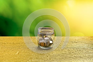 Bottle of cash with coins on wooden table over greeny blur background, for saving and banking finance concept