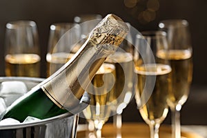 Bottle of champagne in bucket with ice and glasses on blurred background.