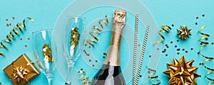 Bottle of champagne with colored glitter, confetti and gift box space for text on colorfull background, top view