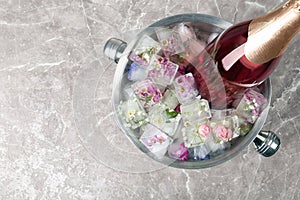 Bottle of champagne with floral ice cubes in bucket on table, top view