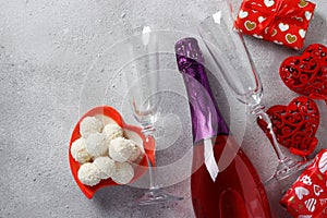 Bottle of champagne, gifts, two glasses and candies on a gray background. Valentine`s day concept. Top view