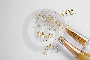 Bottle of champagne, glass with gold glitter and space for text on white background. Hilarious celebration