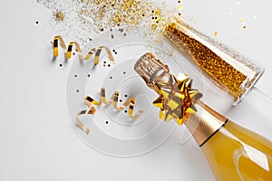 Bottle of champagne and glass with gold glitter on white background, top view. Hilarious