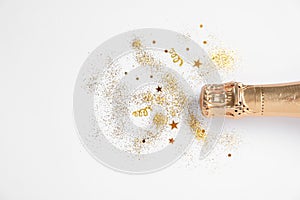 Bottle of champagne with gold glitter and confetti on white background, top view.