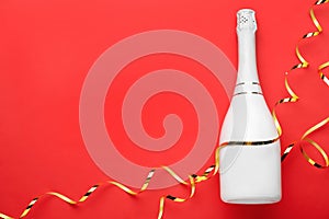 Bottle of champagne and streamers on red background, flat lay. Space for text