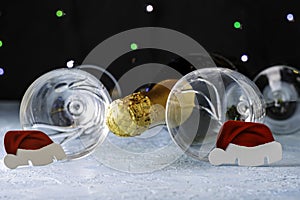 A bottle of champagne and two glass glasses decorated with Santa Claus hats on a black background with backlight