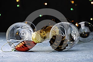 a bottle of champagne and two glass glasses with a pine cone and a Christmas tree toy next to the legs on a black