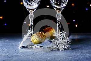 a bottle of champagne and two glass glasses with snowflakes on legs on a black background with backlight