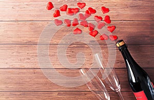 A bottle of champagne, two glass goblets and red hearts flying out of the bottle are on a wooden background. Valentine`s Day theme