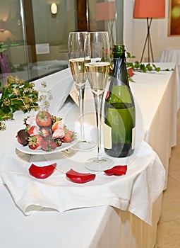 Bottle of champagne, two glasses and chocolate strawberries on a tray with rose petals