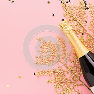 Bottle of champagne wine golden shiny confetti branches pastel pink background. Copy space. Festive minimalism concept.