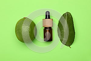 Bottle of citrus essential oil, fresh lime and leaf on green background, flat lay