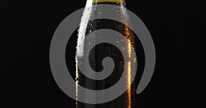 Bottle of cold beer on a black background. It slowly rotates. Condensate