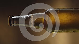 A bottle of cold beer slowly rotates against a dark background. Cold light beer close-up