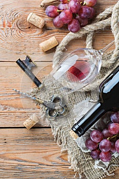 Bottle, corkscrew, glass of red wine, grapes on a table