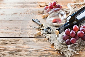 Bottle, corkscrew, glass of red wine, grapes on a table