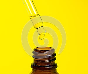 Bottle of cosmetic oil with a pipette on a yellow background. Close up liquid drop dripping. Beauty, medicine and  health care