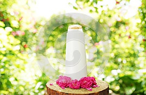 Bottle with cosmetic product: lotion or shampoo with fresh herbs and flowers on natural background, top view. Beauty, skin, hair