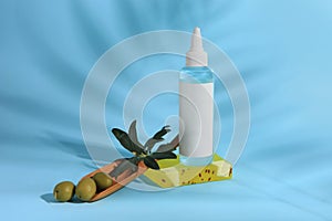 Bottle of cosmetic product, soap bar and olives on light blue background