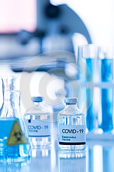 Bottle of COVOD-19 vaccine sample in a laboratory with lab equipment in blur background. Idea for researching and lab tests for