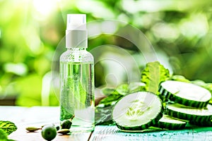 Bottle of cucumber oil sits next to freshly sliced cucumbers on a wooden surface. Organic cosmetics concept. Copy space