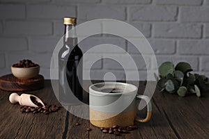Bottle with delicious syrup, mug of aromatic coffee and beans on wooden table