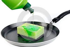 Bottle of dish washing liquid flows on sponge on pan over white background.