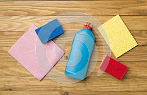 Bottle with dishwashing detergent and sponges on wooden background, top view