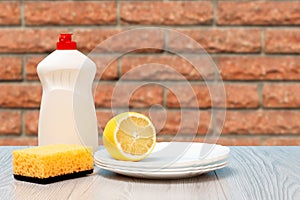 Bottle of dishwashing liquid, sponge, plates and lemon on blue background.