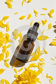 Bottle with dropper pipette with serum or essential oil on the background yellow flower petals.