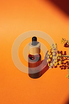 Bottle with dropper pipette with serum or essential oil. Orange background with daylight and yellow flowers.