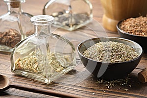 Bottle of dry herbs for making healing infusion or tincture. Bowls of medicinal plants and wooden mortar on background.