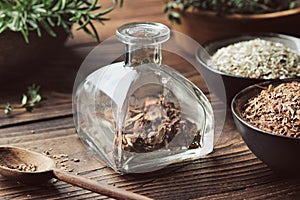 Bottle of dry medicinal bark and herbs for making healing infusion or tincture. Bowls of dried medicinal plants and wooden mortar