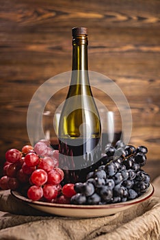 Bottle of dry red wine with a glass and a bunch of grapes on a wooden table. Concept of viticulture and winemaking