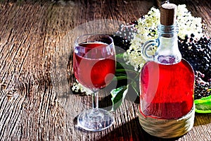 Bottle with elderberry juice and fresh berry fruits on wooden table.