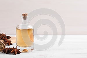 Bottle of essential oil, anise and seeds on white wooden table. Space for text