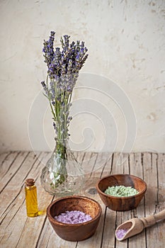 Bottle with essential oil and bowls with sea salt on wooden table. Lavender cosmetics, spa and aromatherapy