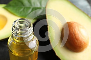 Bottle of essential oil and cut avocado on table, closeup