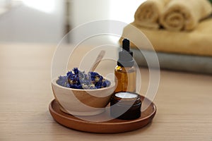 Bottle of essential oil, dry flowers and jar with cream on light wooden table. Spa therapy