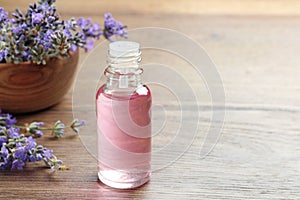 Bottle of essential oil and  flowers on wooden table. Space for text