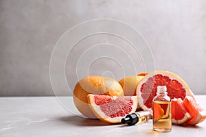 Bottle of essential oil and grapefruits on grey table