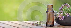 bottle of essential oil and  lavender flowers in a bowl  on a wooden table and green background